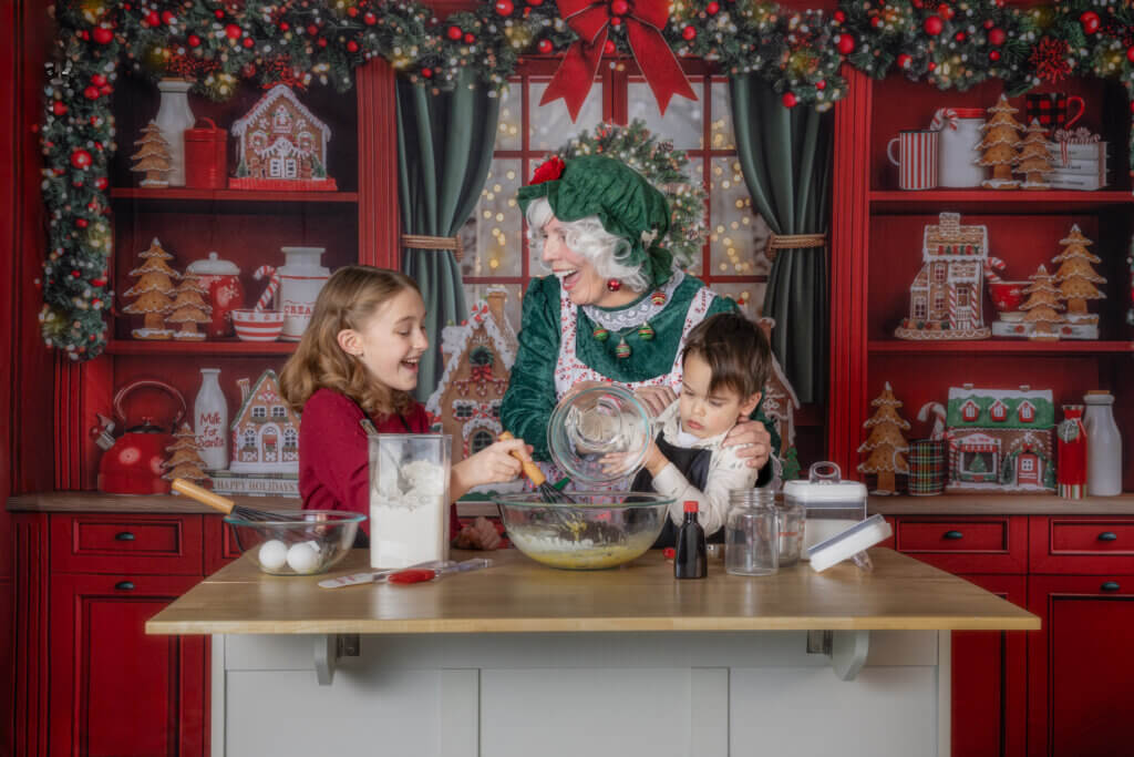 Two children laughing and baking cookies with Mrs. Claus during a Santa photo session in Colorado Springs holiday studio.