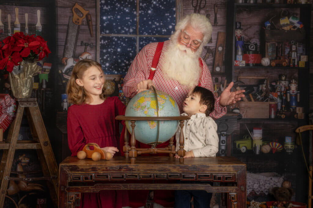 Santa Claus showing a globe to two children in his toy workshop during a Christmas photo session in Colorado Springs.