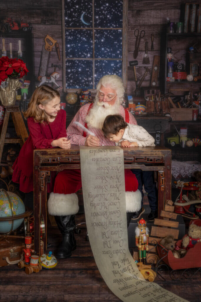 Santa Claus showing a globe to two children in his toy workshop during a Christmas photo session in Colorado Springs.