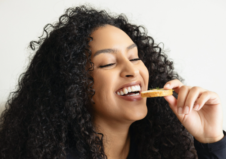 Smiling woman eating a cracker.